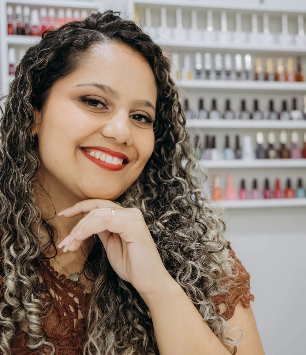 Beatriz Emiliano sorrindo em frente à parede de esmaltes do estúdio